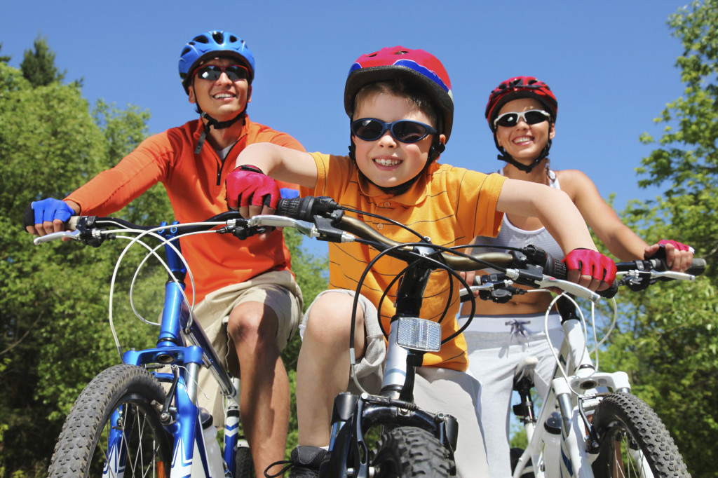 Portrait of happy boy riding bicycle in the park with his parents following close behind